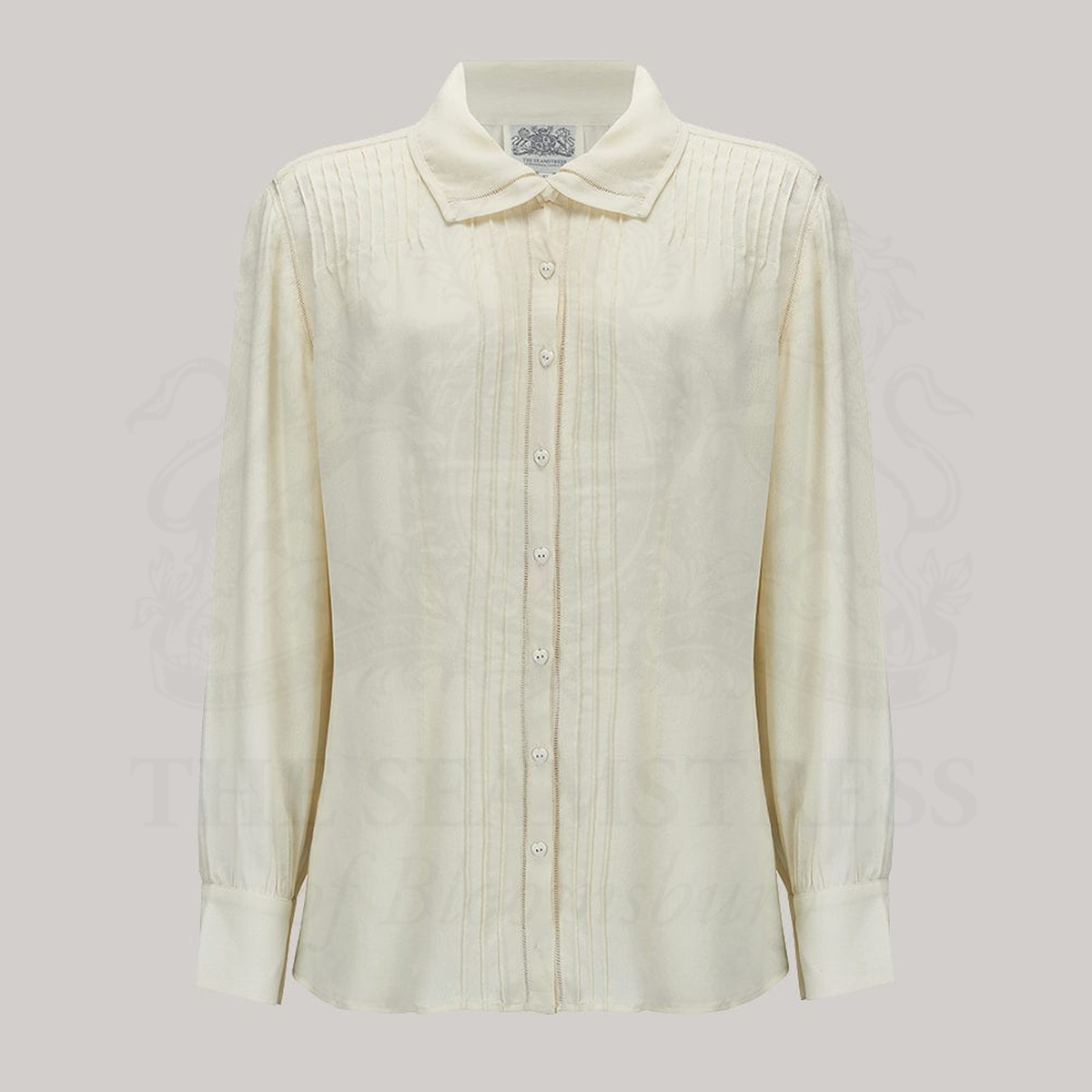 A 1940s style cream long sleeve blouse. Detailed pin tuck stitching down the front and back of the blouse, heart shaped buttons, and long sleeves with deep cuffs. Blouse has a cutaway collar with more pin tuck stitching. 
